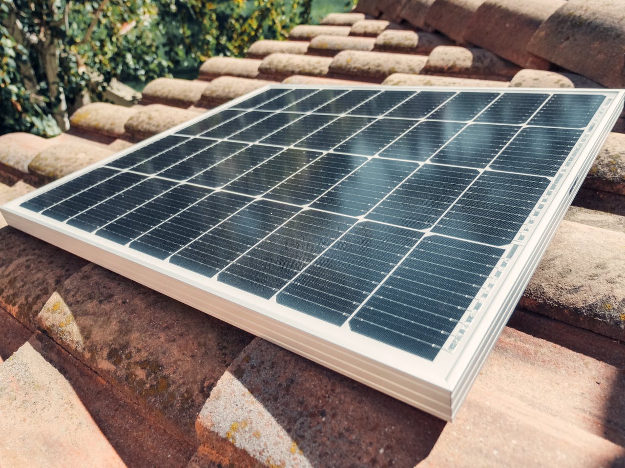 Close-up of a solar panel installed on rooftop tiles under bright daylight, emphasizing renewable energy.