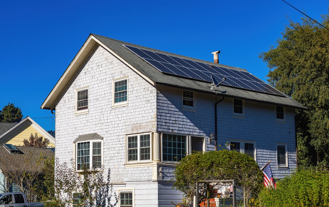 A modern two-story home with solar panels on its roof under a clear blue sky.