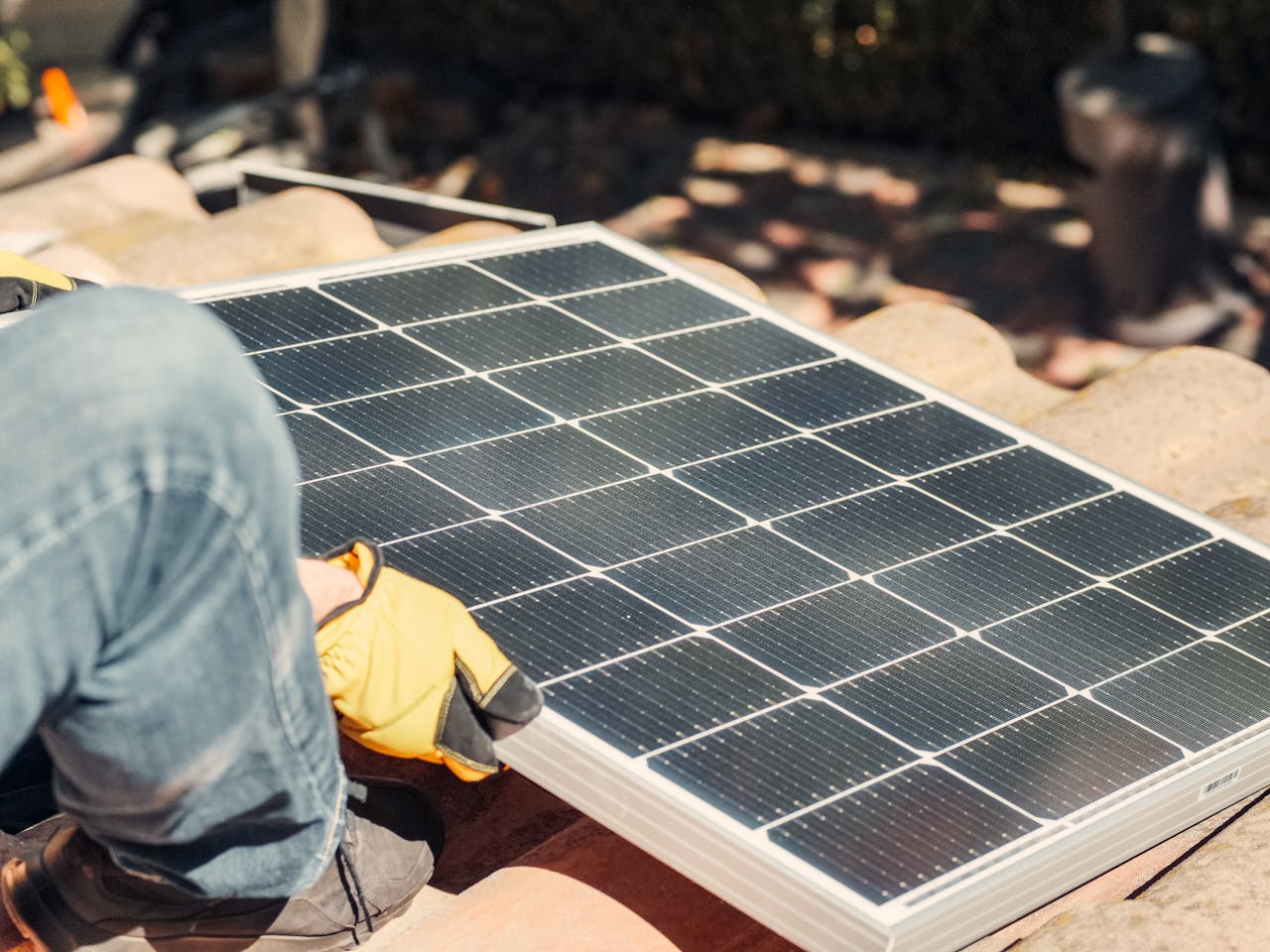 A worker installs a solar panel on a sunlit rooftop, exemplifying renewable energy.